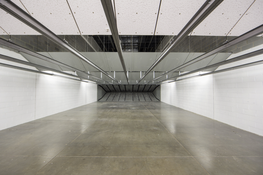 Wide view down the firing lanes of a commercial indoor shooting range with overhead industrial lighting and bullet traps at the far end