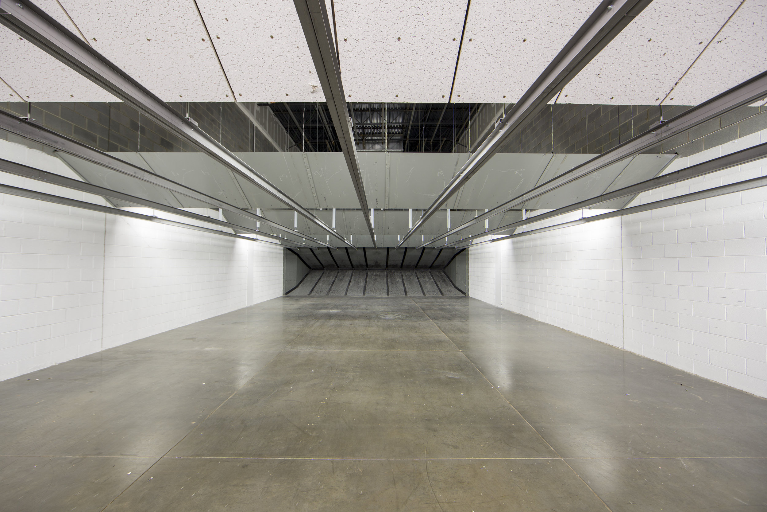 Wide view down the firing lanes of a commercial indoor shooting range with overhead industrial lighting and bullet traps at the far end