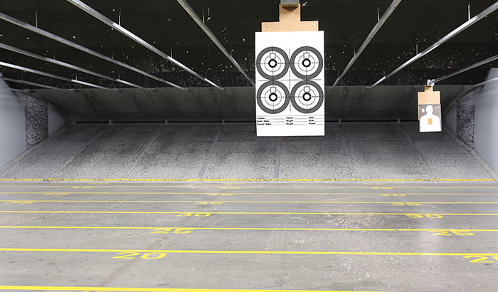 Downrange view of a paper target on the lane with numbered distance markers and overhead industrial lighting