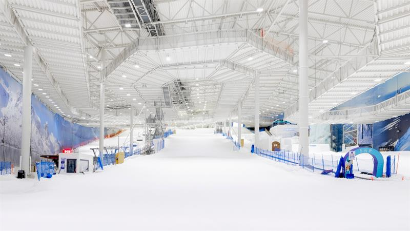 Wide angle view of an indoor ski slope at full lighting load with high-bay fixtures illuminating the entire run from top to base