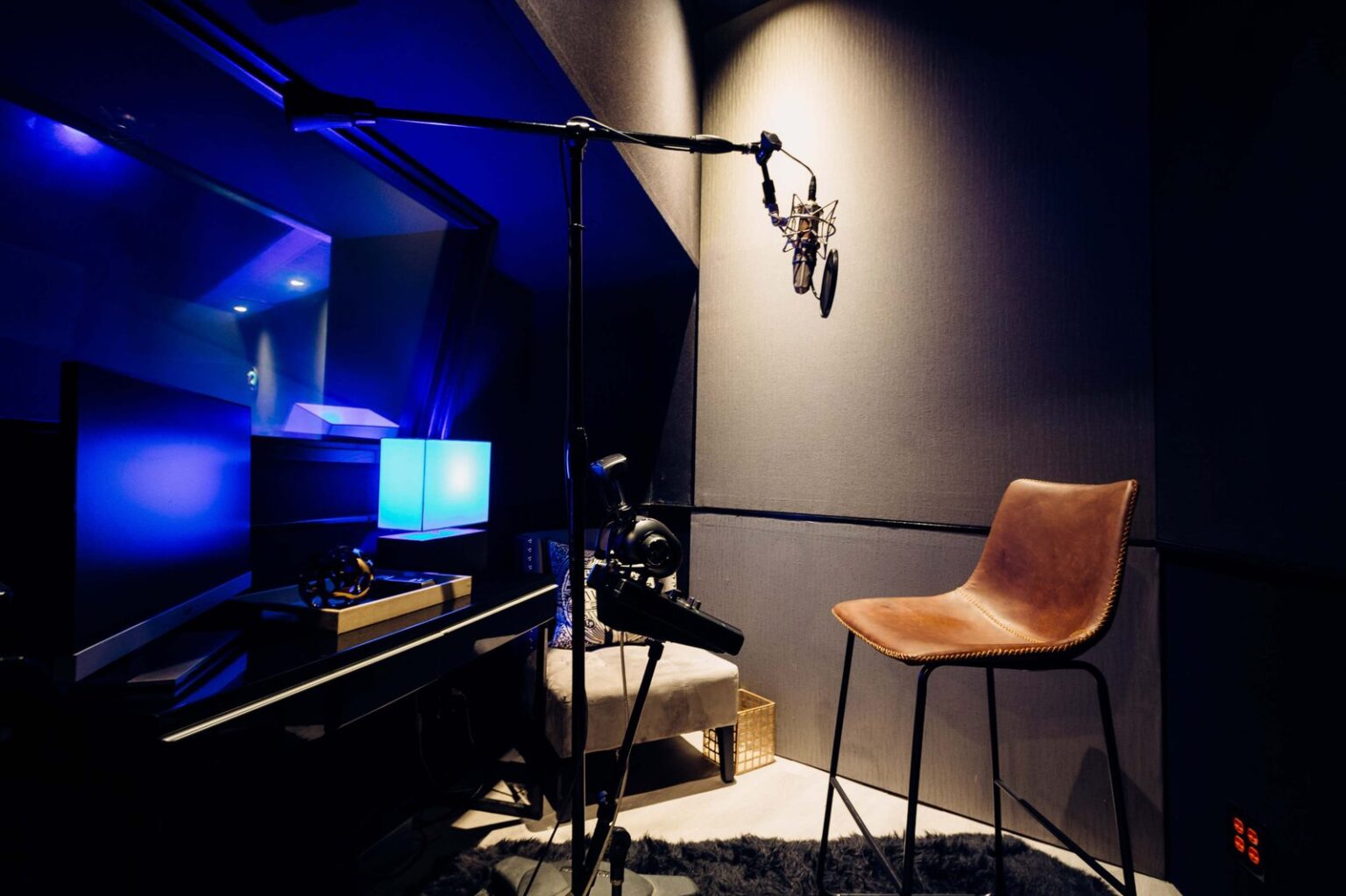 Singer wearing headphones standing at a professional microphone inside a dimly lit vocal booth with warm ambient lighting