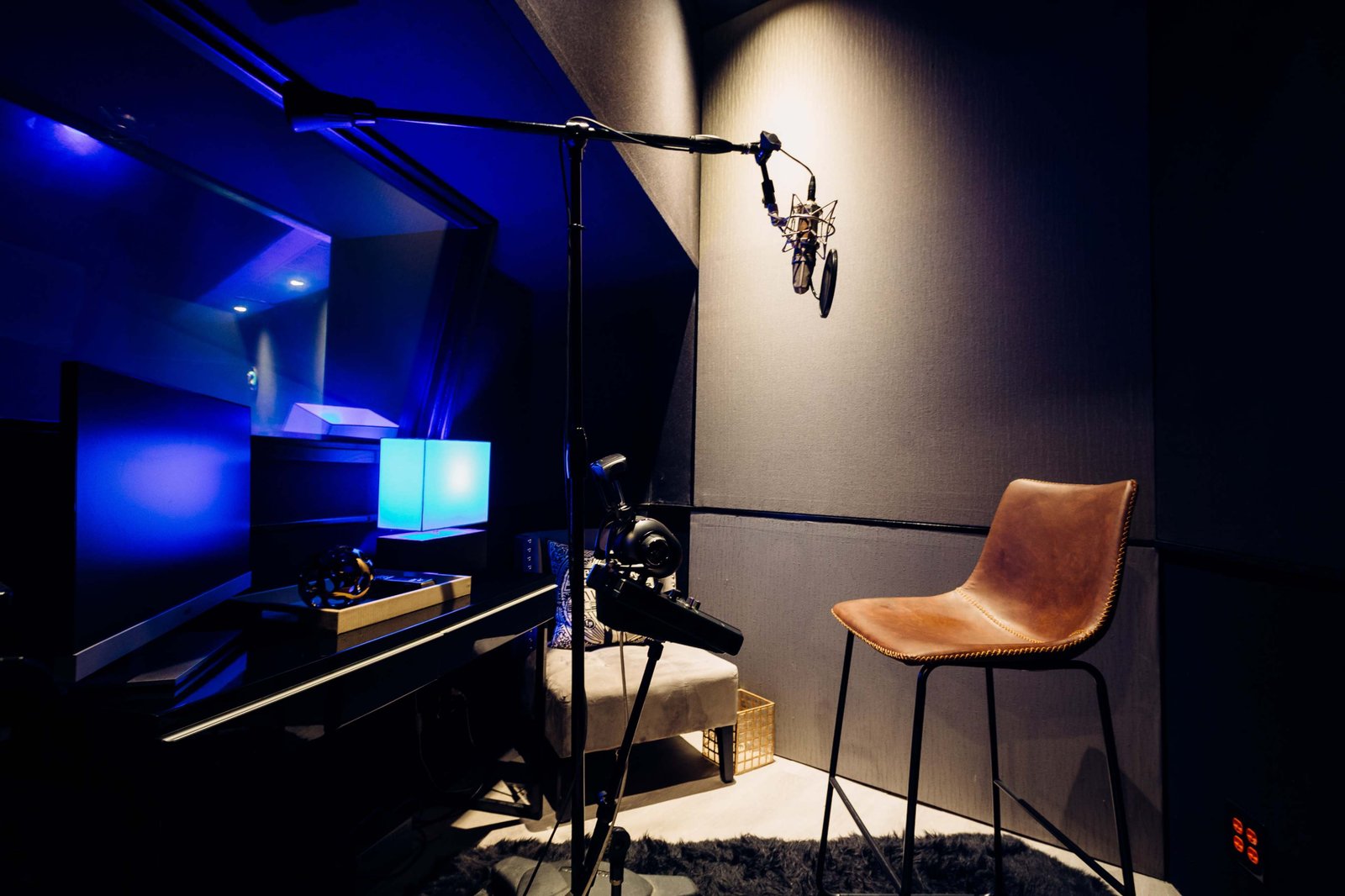 Singer wearing headphones standing at a professional microphone inside a dimly lit vocal booth with warm ambient lighting